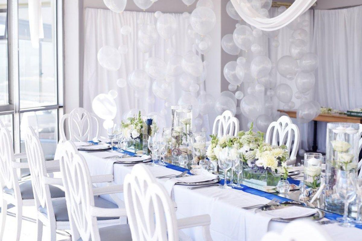 A long table with white chairs and balloons on the wall.