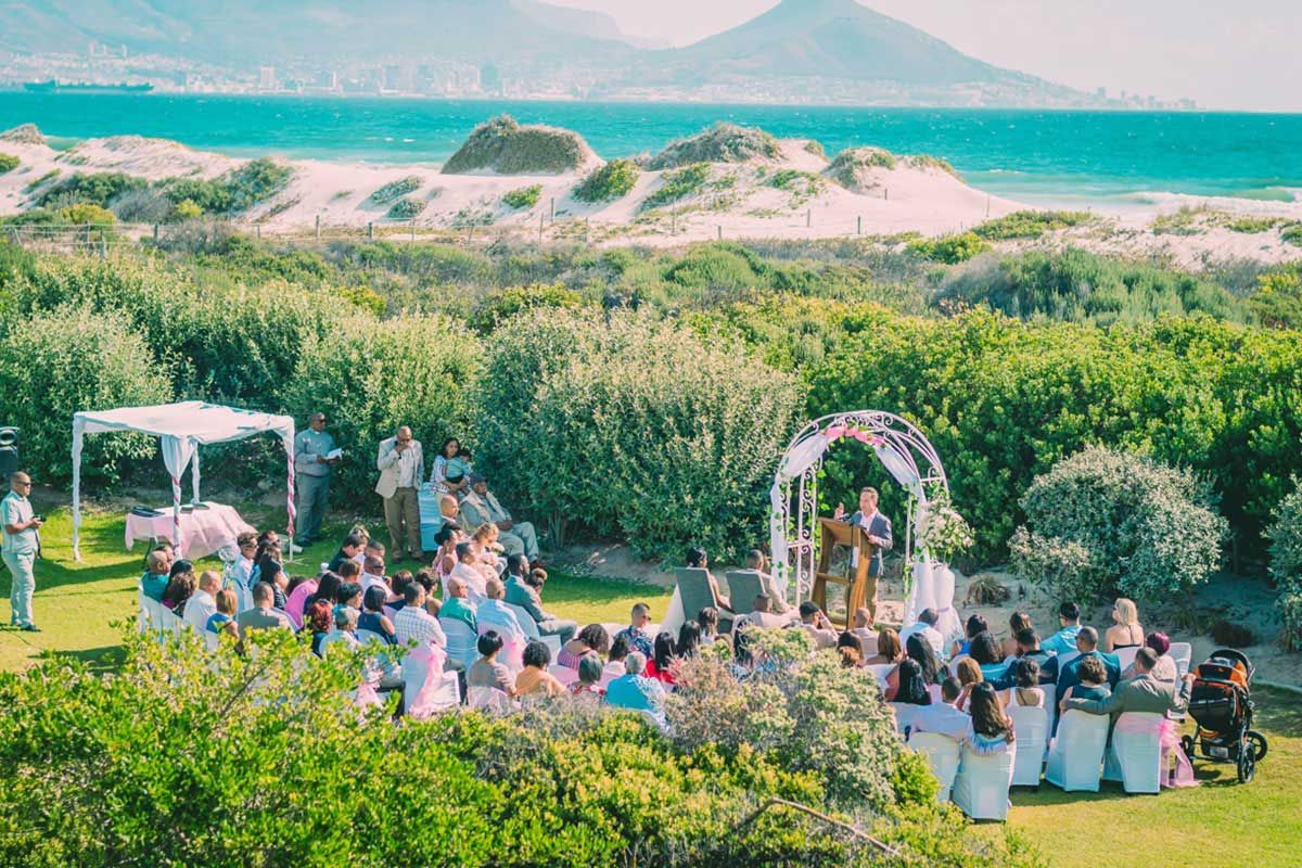 A group of people are sitting in a field at a wedding ceremony.
