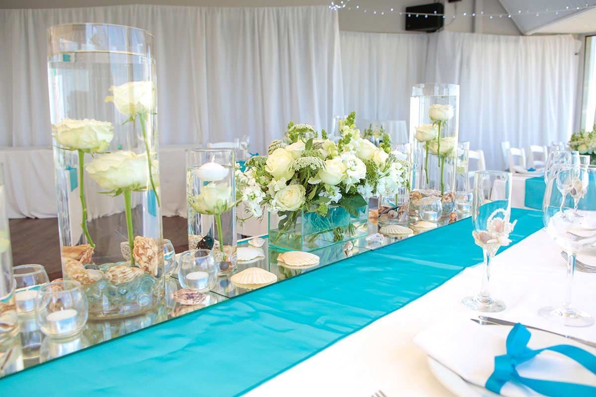 A long table with a blue table runner and vases of flowers on it.