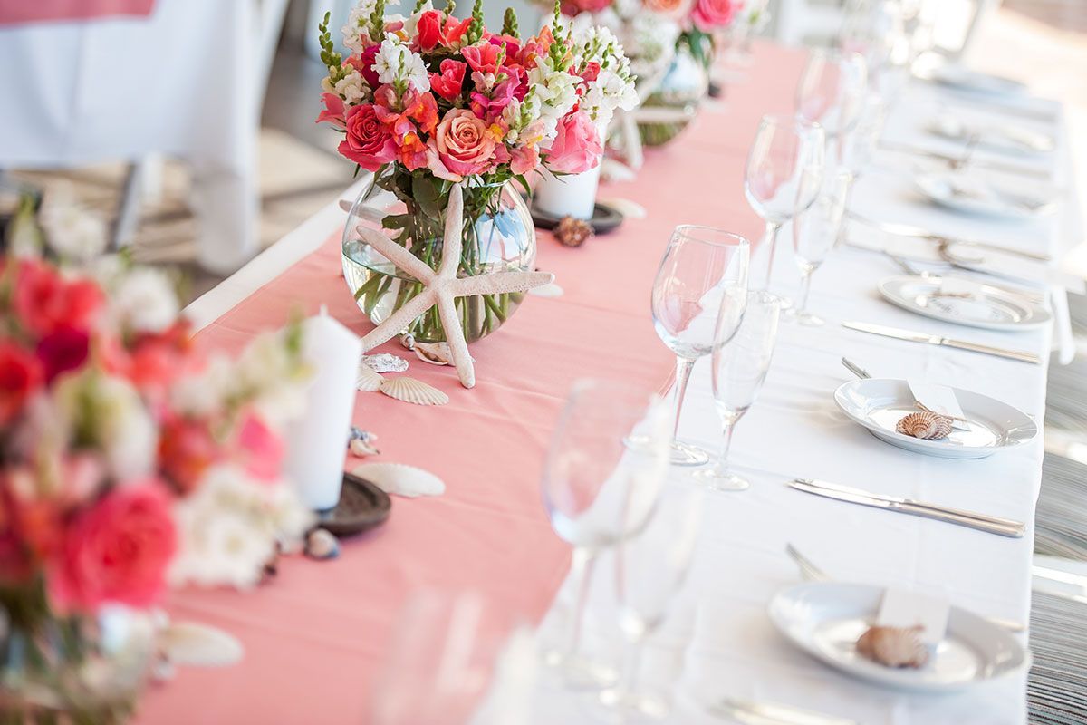 A long table with plates , utensils , and flowers on it.