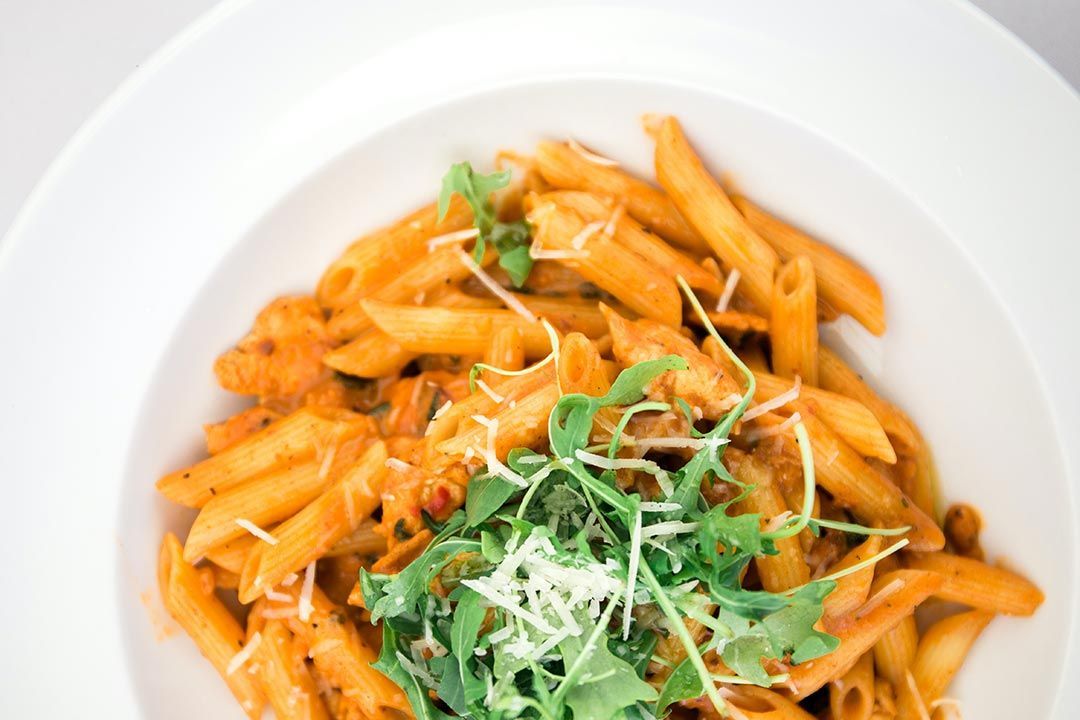 Primo piano di un piatto bianco con sopra pasta e verdure.