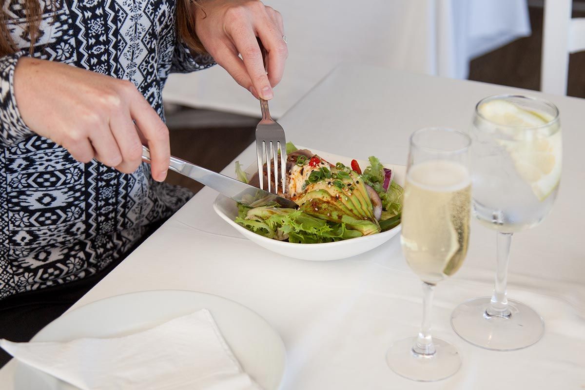 A woman is sitting at a table eating a salad with a fork.