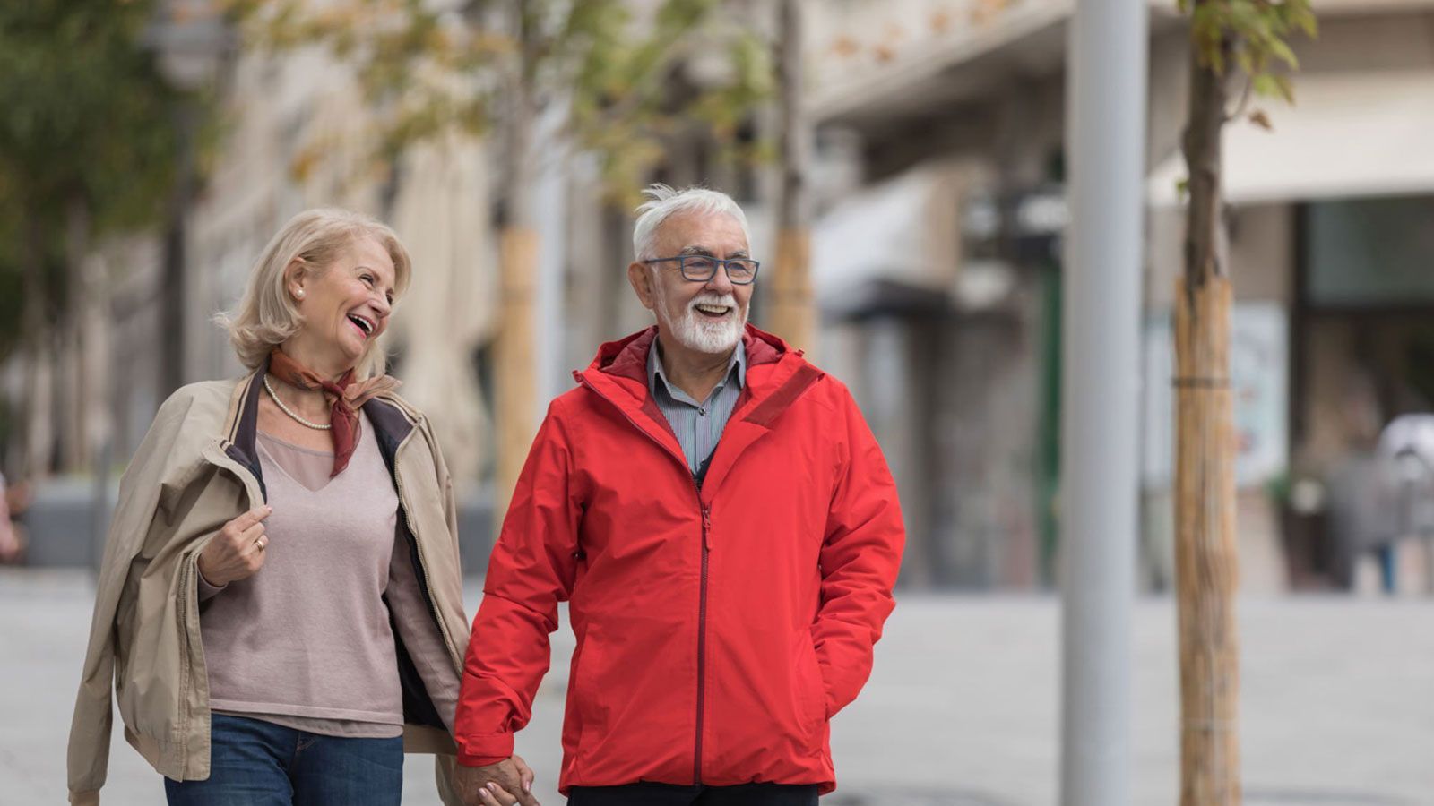 An elderly couple is walking down the street holding hands.