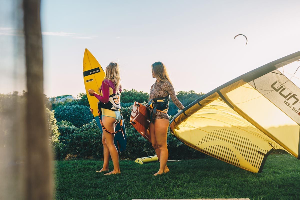 Due donne sono in piedi sull'erba con una tavola da surf e un aquilone.