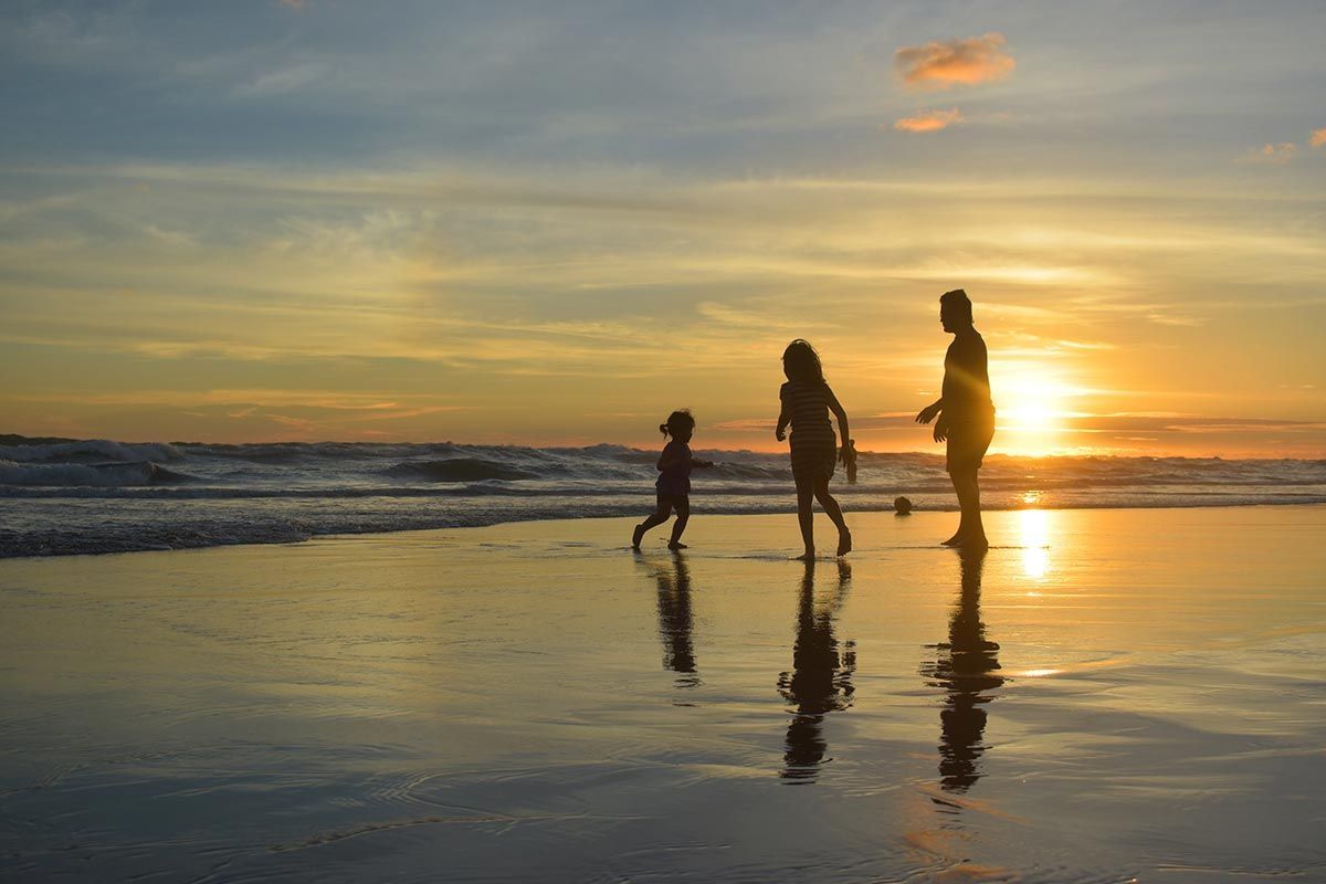 Een gezin wandelt over het strand bij zonsondergang.