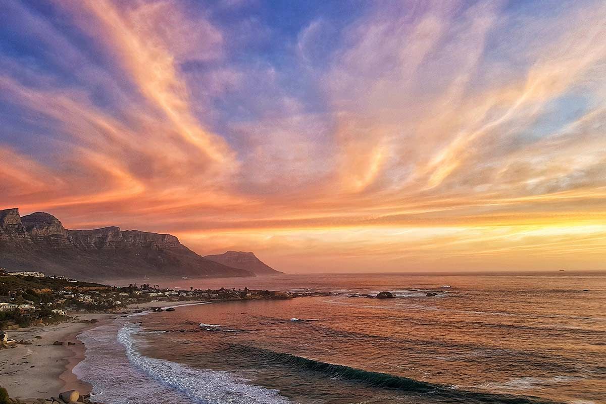 There is a sunset over the ocean with a mountain in the background.