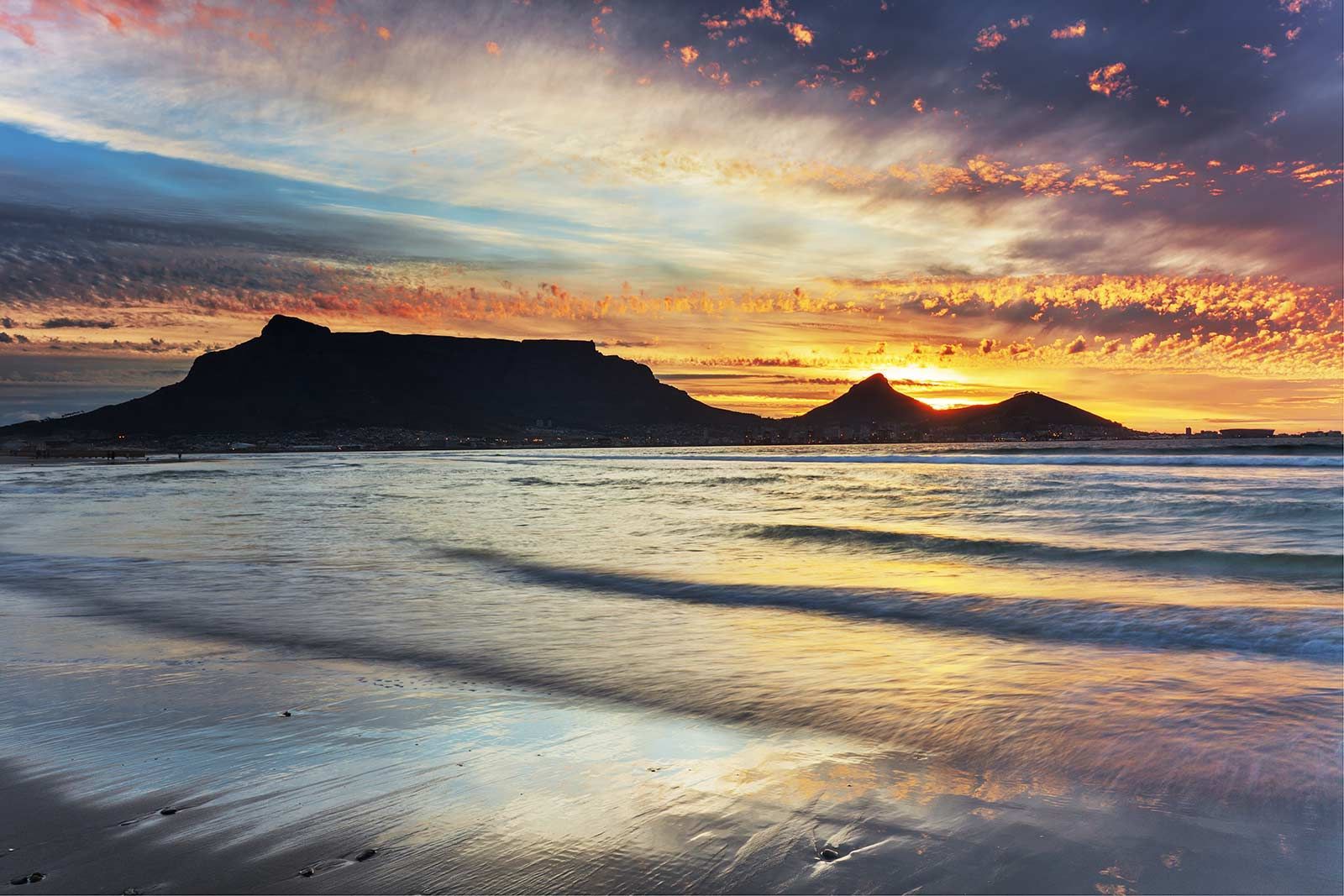 Een zonsondergang boven een strand met een berg op de achtergrond.