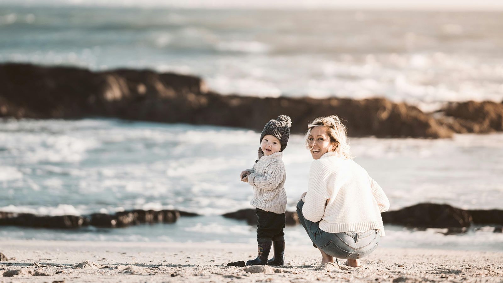 A woman and a child are kneeling on the beach near the ocean.