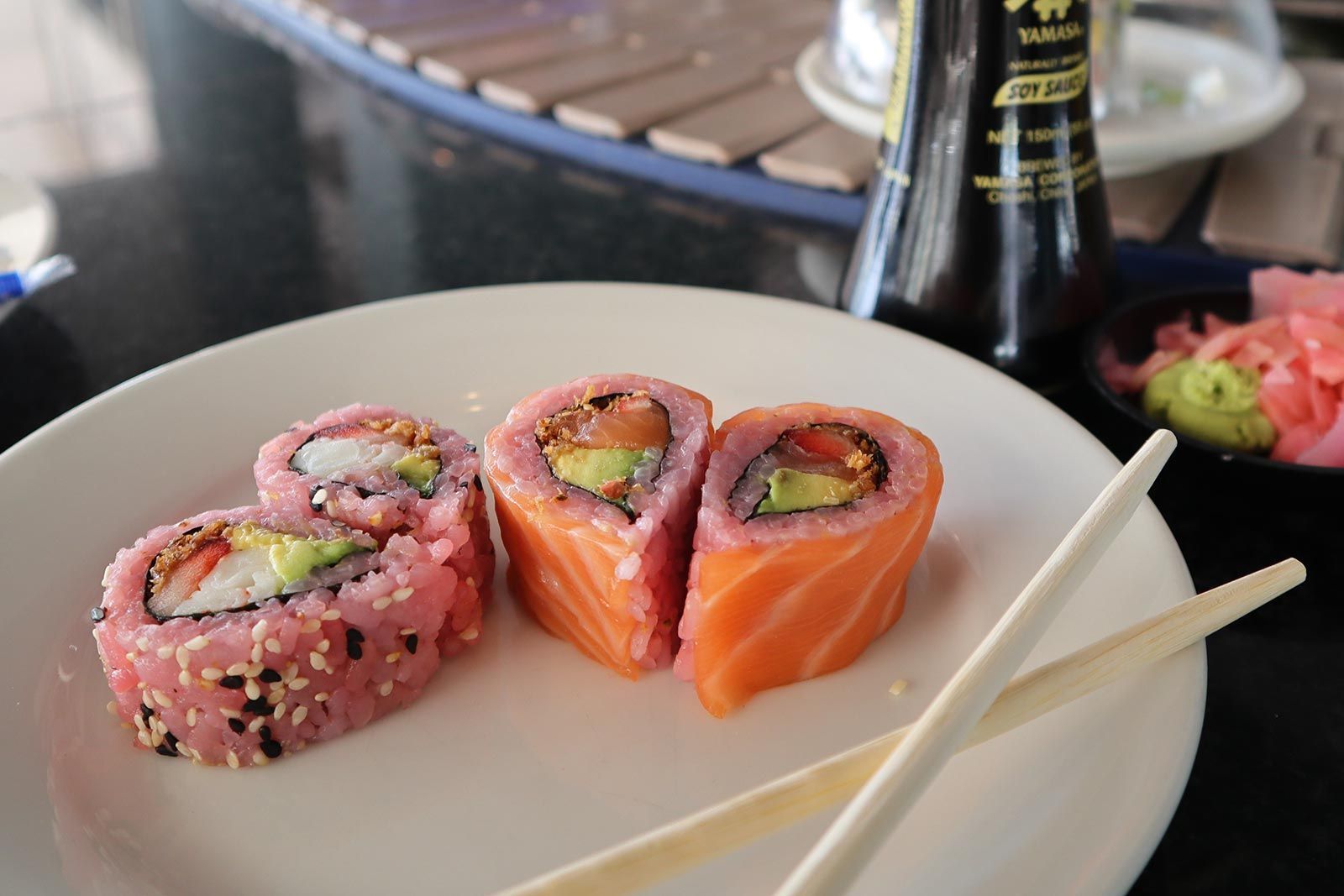 A plate of sushi with chopsticks and a bottle of soy sauce in the background