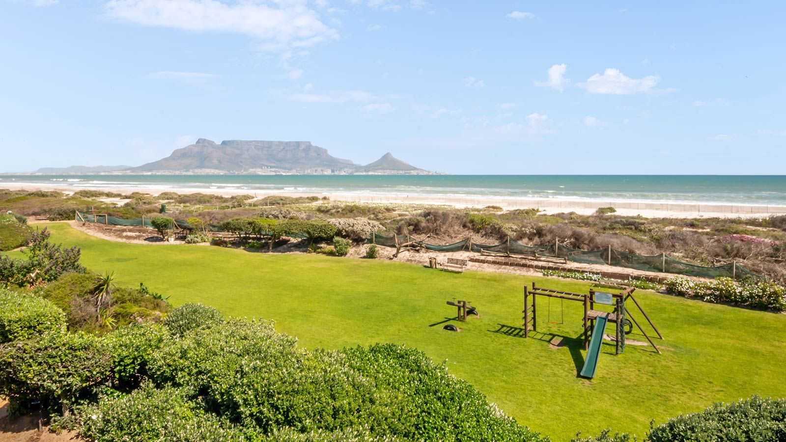 Ein Blick auf einen Strand mit einem Spielplatz im Vordergrund und einem Berg im Hintergrund.