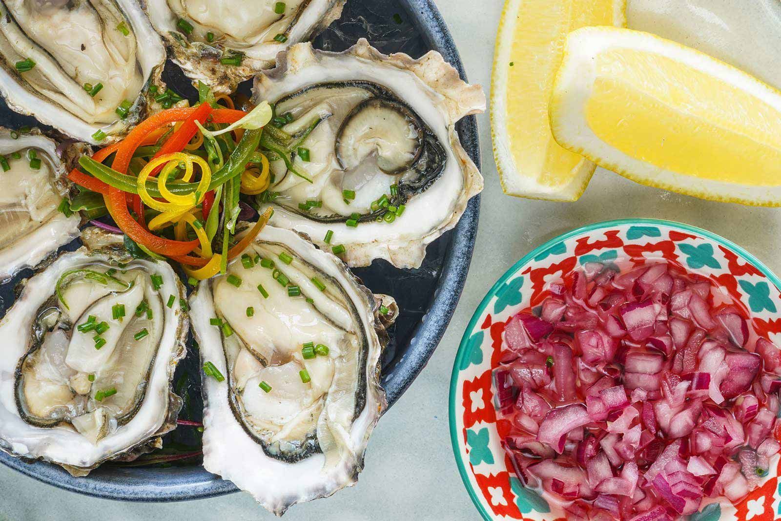 Un plato de ostras junto a un bol de cebollas y una rodaja de limón.