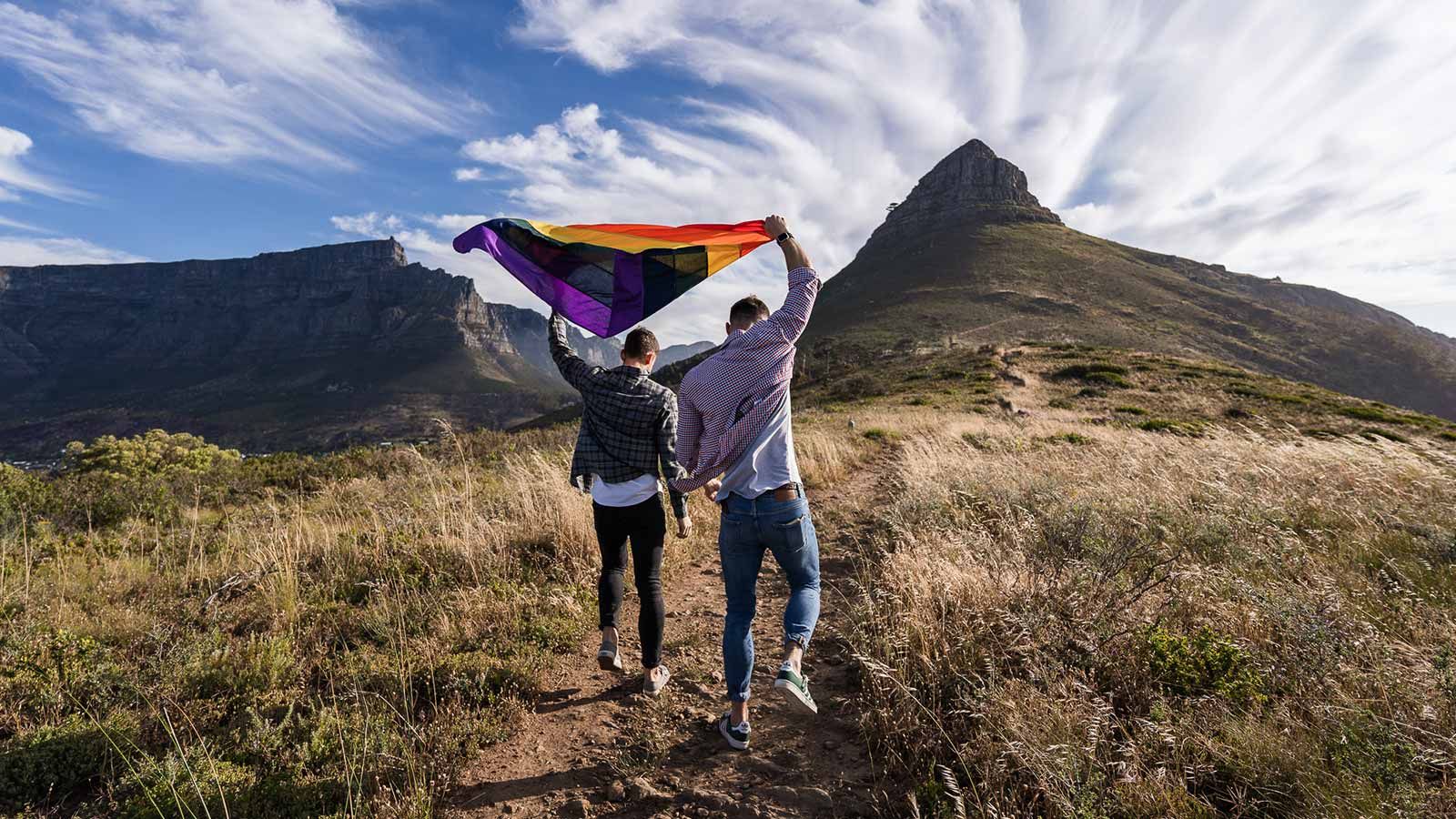 Een man en een vrouw houden een regenboogvlag vast voor een berg.