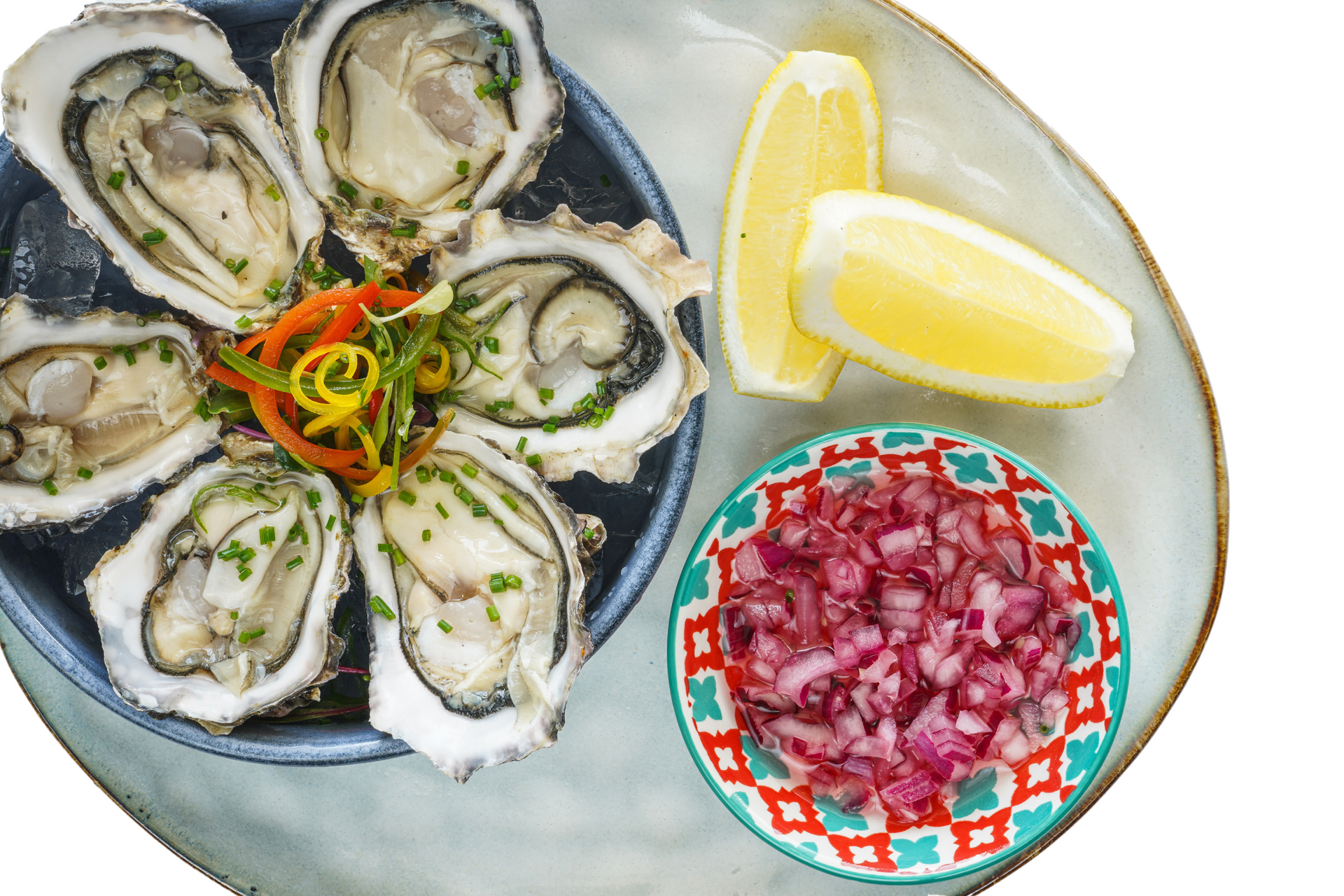 A bowl of oysters with lemon and onions on a plate.