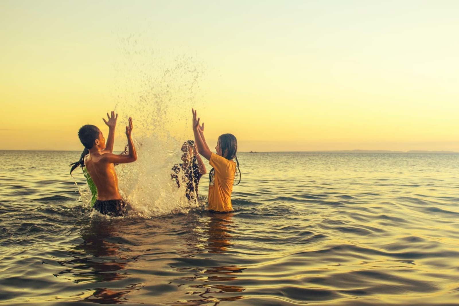 Een groep kinderen speelt in de oceaan bij zonsondergang.