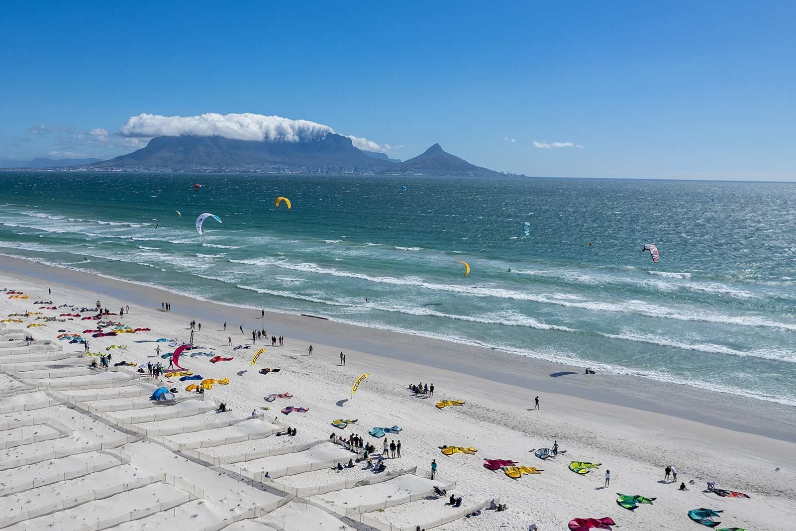 Una spiaggia con una montagna sullo sfondo e un sacco di gente su di essa