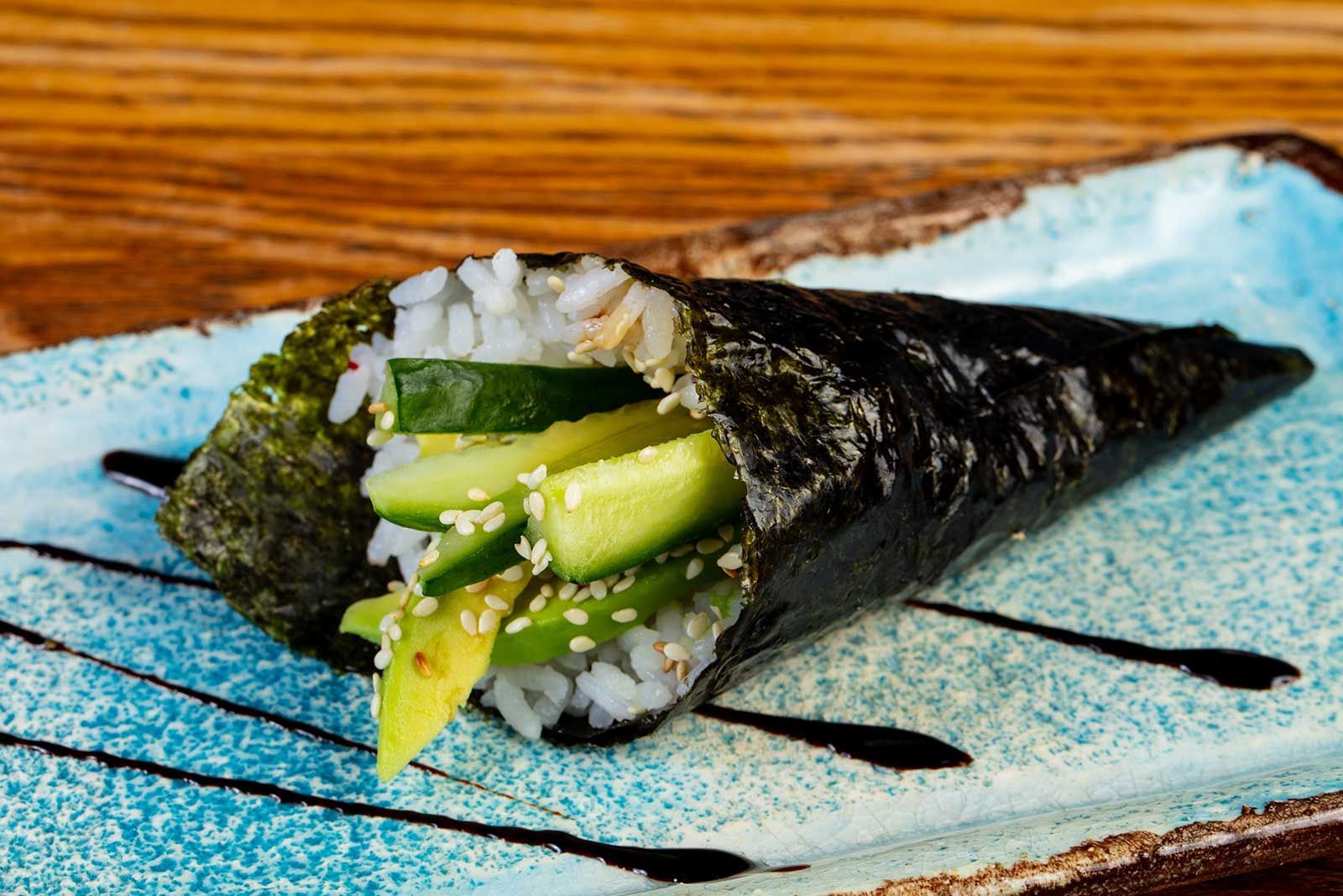 A close up of a sushi cone with cucumber and rice on a plate.