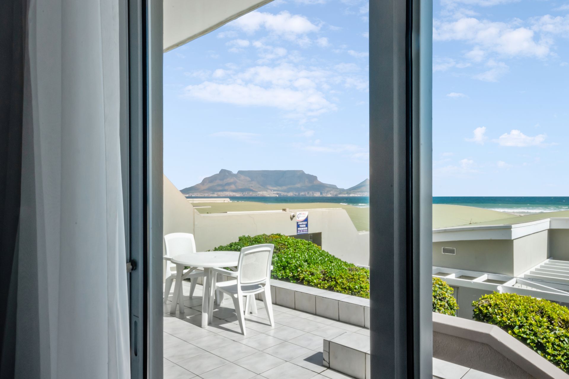 A view of the ocean from a hotel room with a table and chairs.