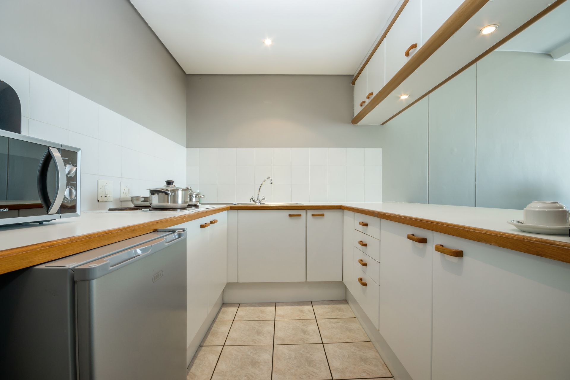 A kitchen with white cabinets , a refrigerator , a microwave and a sink.