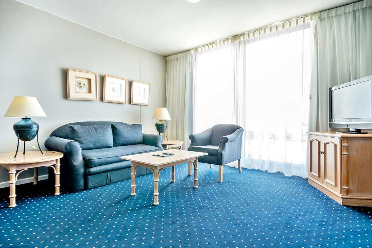 Ein Wohnzimmer mit Couch, Sessel, Tisch und Fernseher.