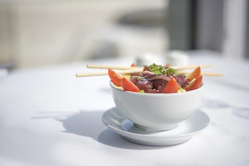 A bowl of salad with chopsticks on a saucer on a table.