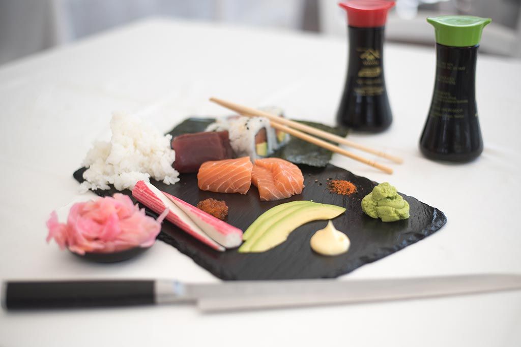 Een bord sushi met eetstokjes en sausjes op een tafel.