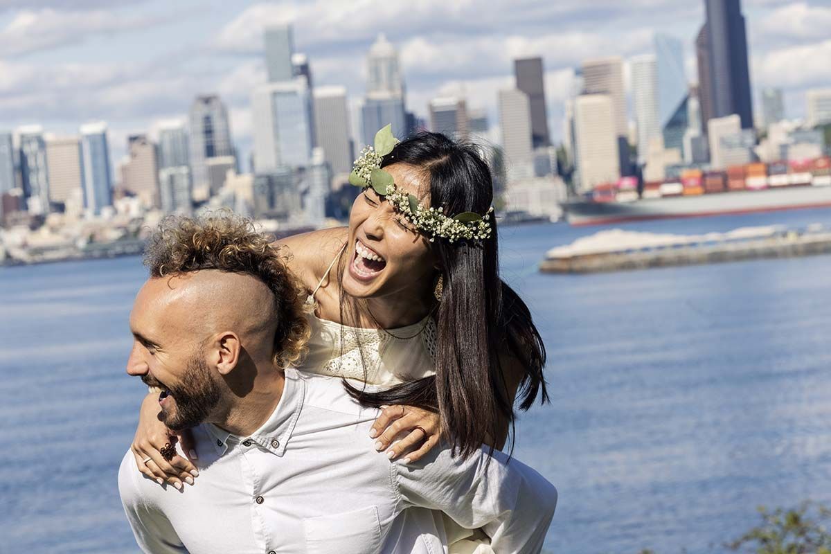 A man is carrying a woman on his back in front of a city skyline.