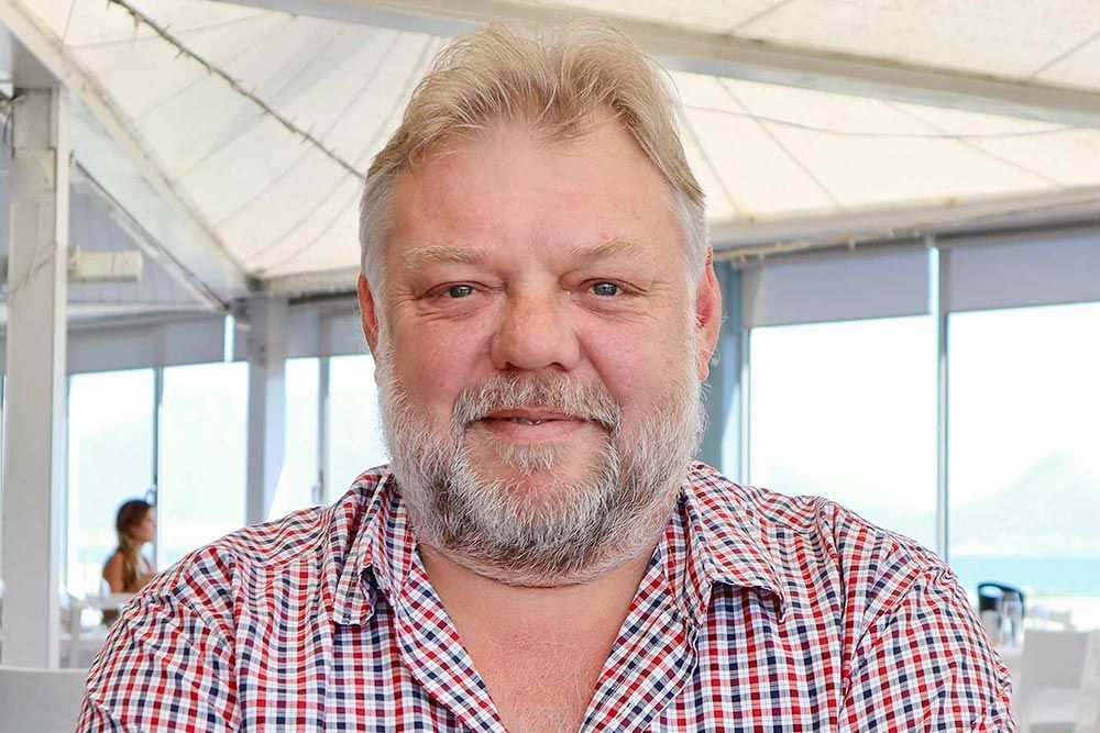 Un uomo con la barba indossa una camicia a quadri e sorride.