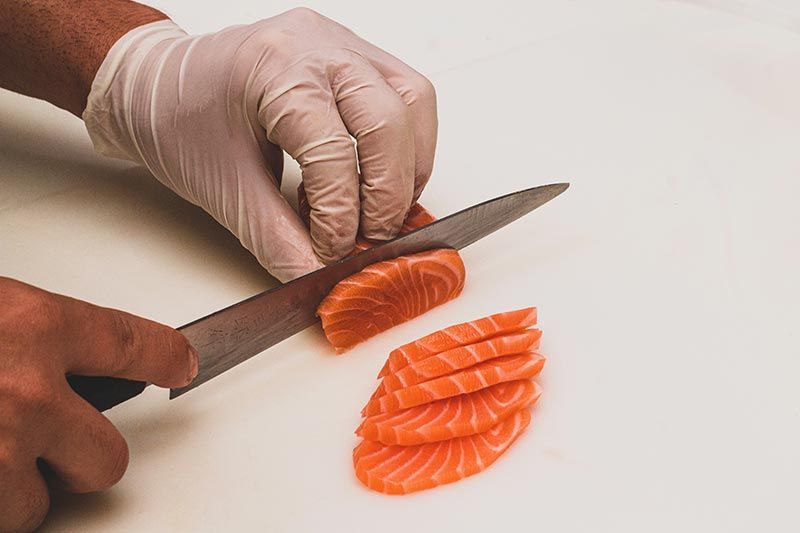 Iemand met handschoenen aan snijdt een stuk zalm op een snijplank.