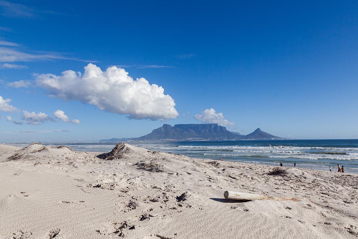 Ein Strand mit einem Berg im Hintergrund und einer Wolke am Himmel.