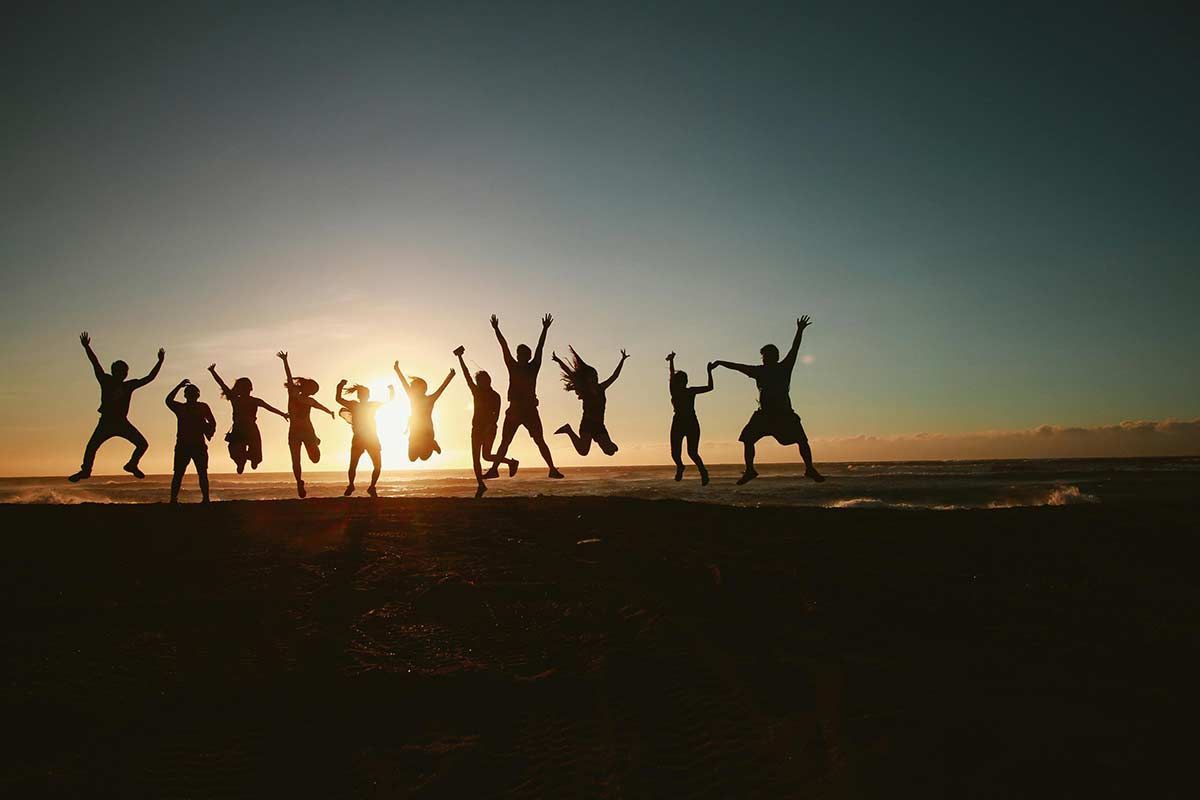 A group of people are jumping in the air on a beach at sunset.