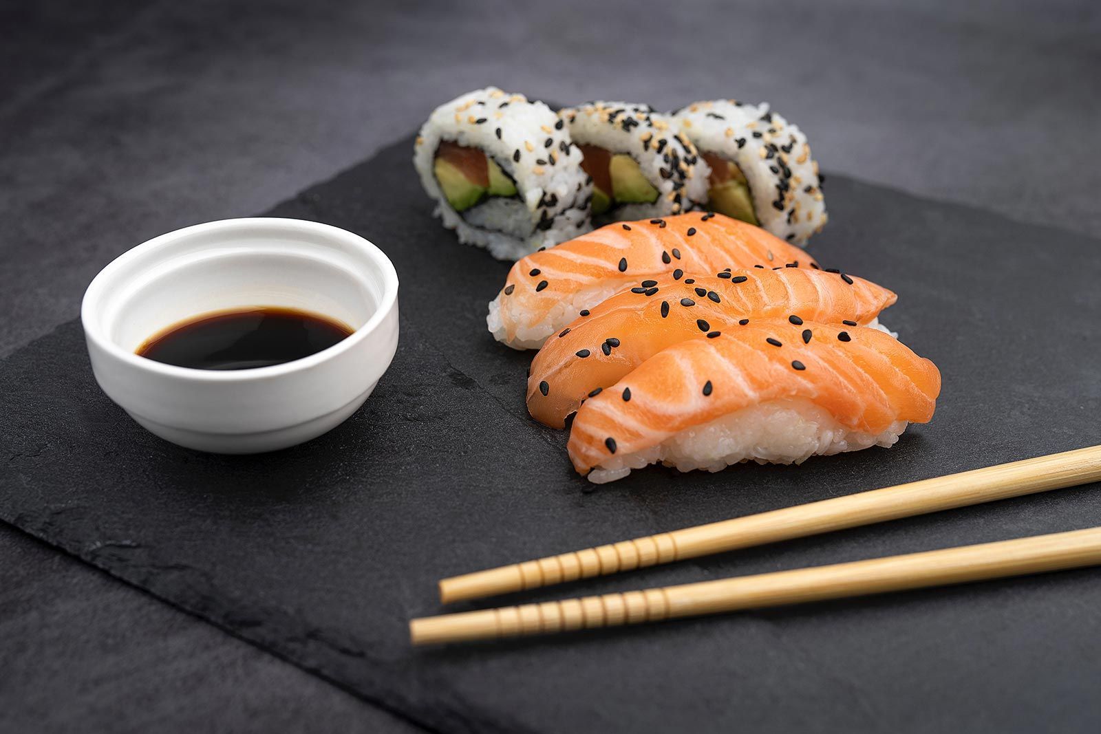 A plate of sushi with chopsticks and a bowl of soy sauce.