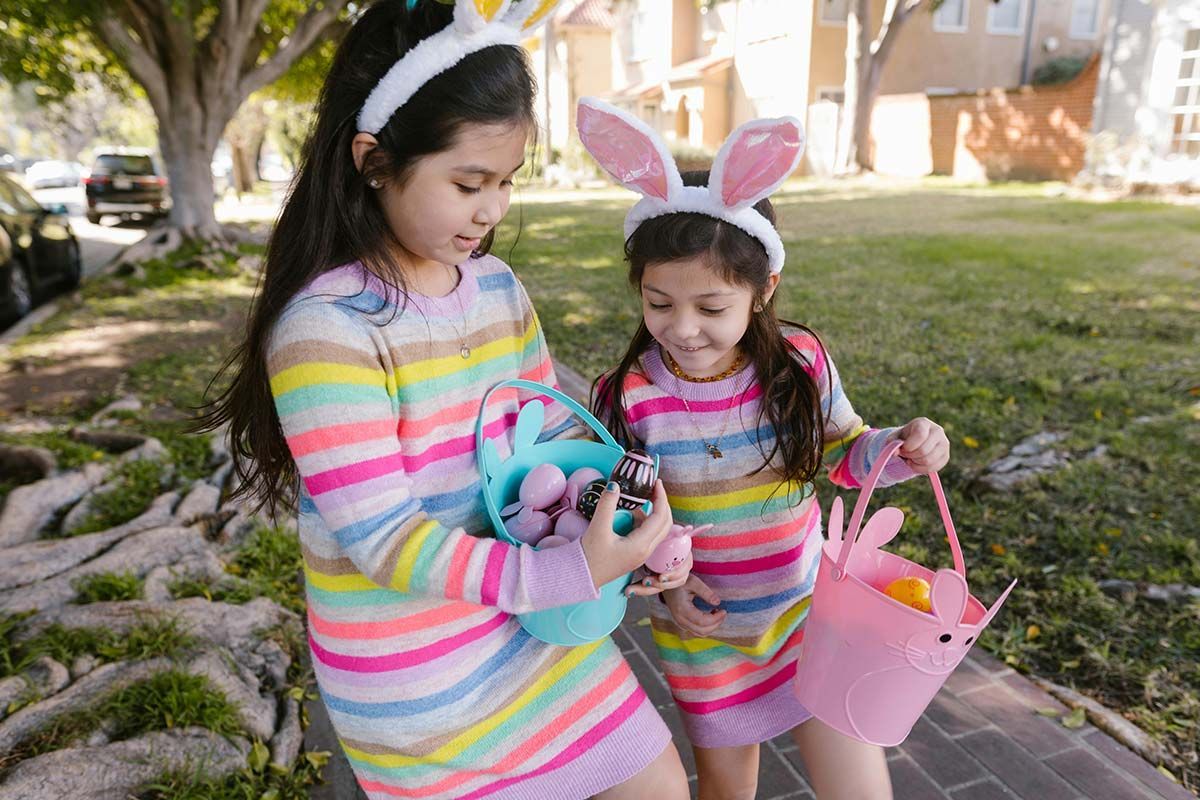 Due bambine indossano orecchie da coniglio e tengono in mano cestini pasquali.