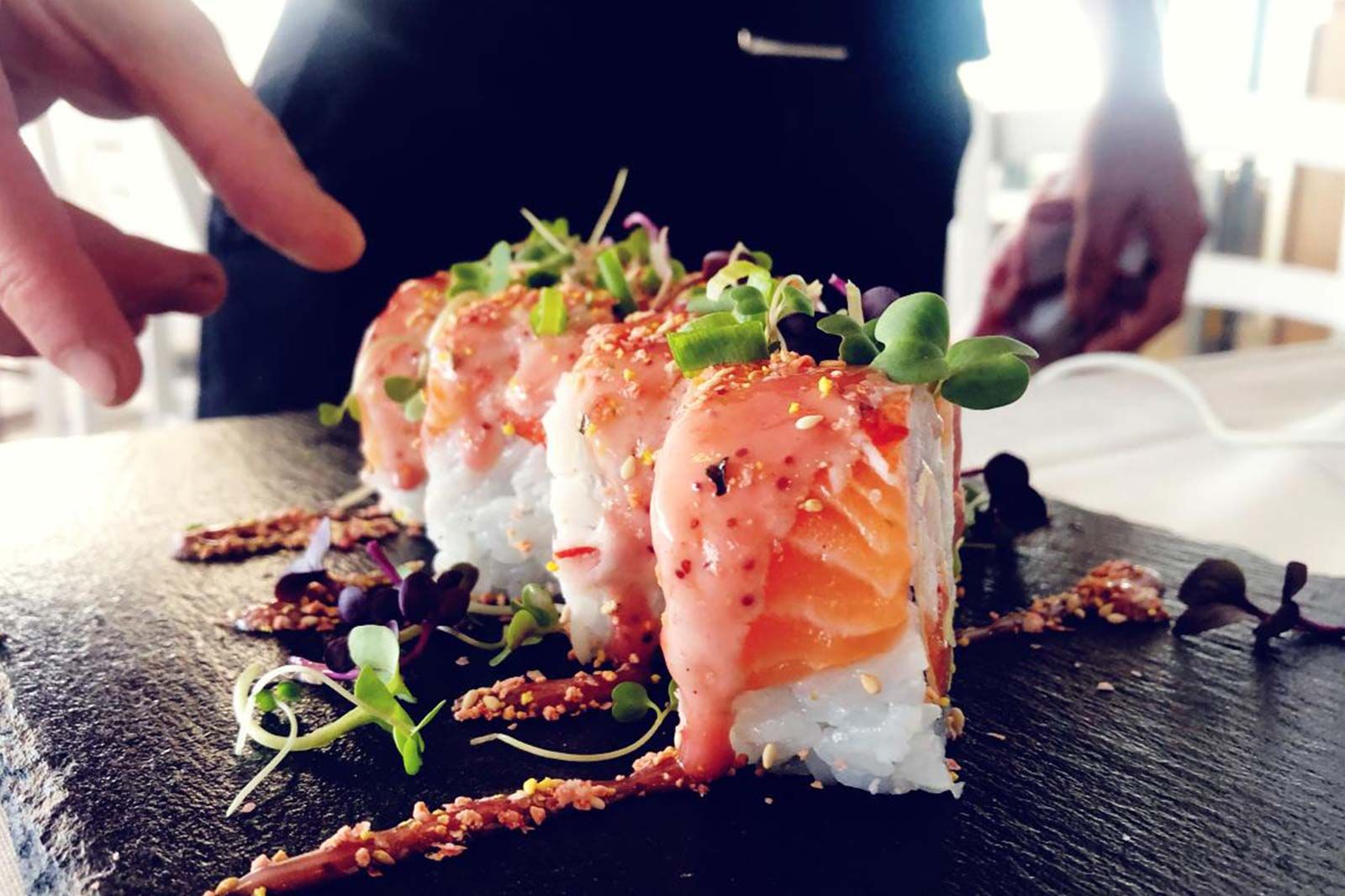 A person is touching a plate of sushi with their finger