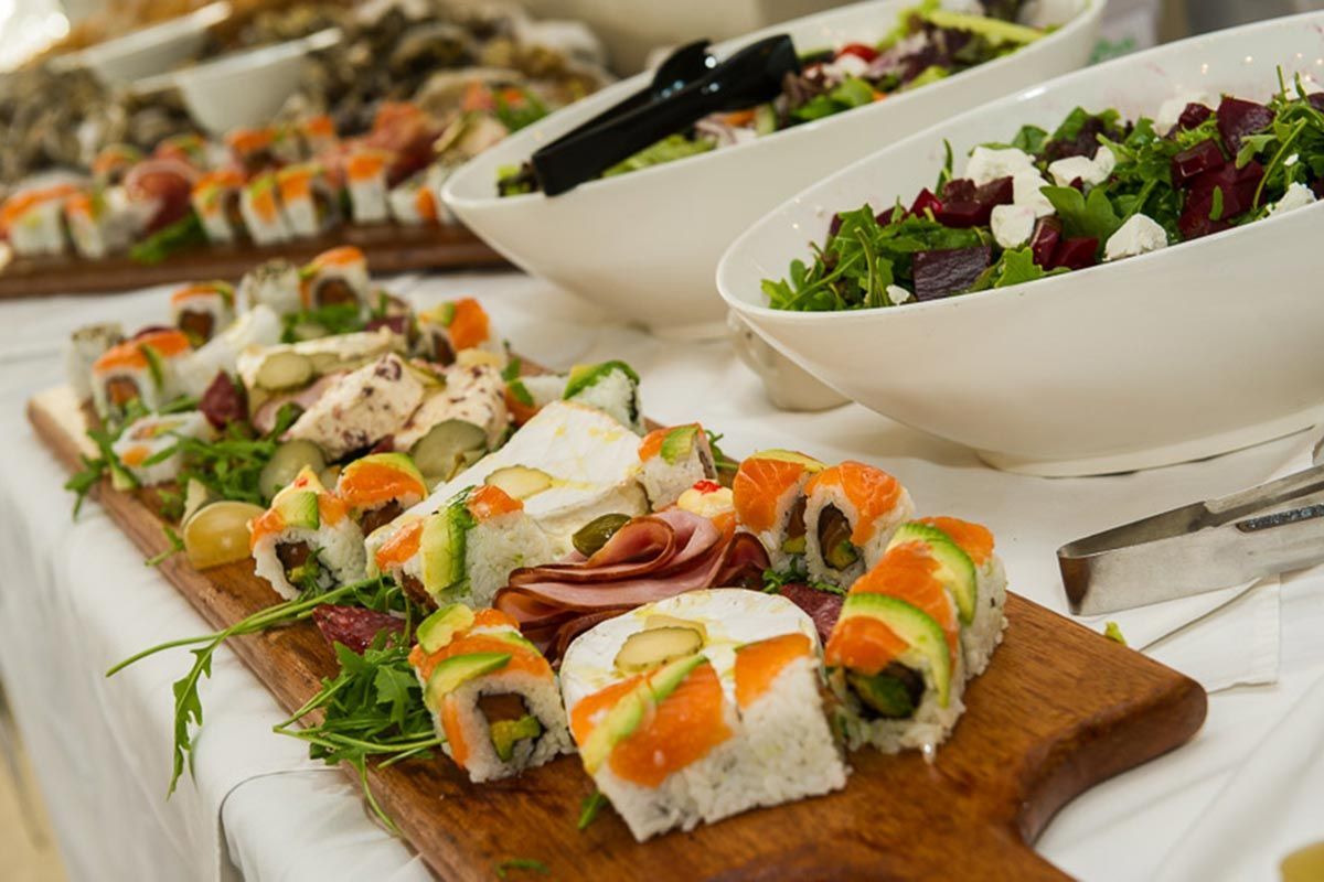 A wooden cutting board topped with sushi and salads on a table.