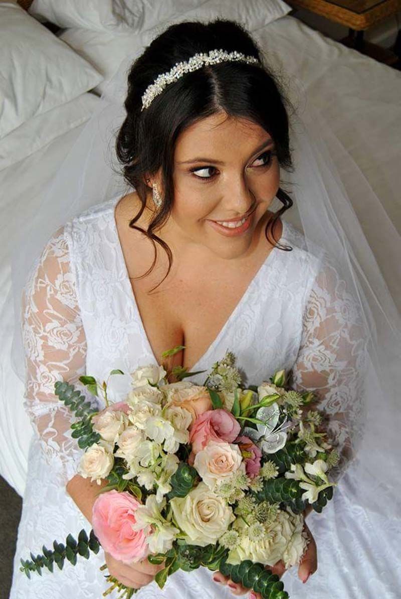 A bride in a white dress is sitting on a bed holding a bouquet of flowers.