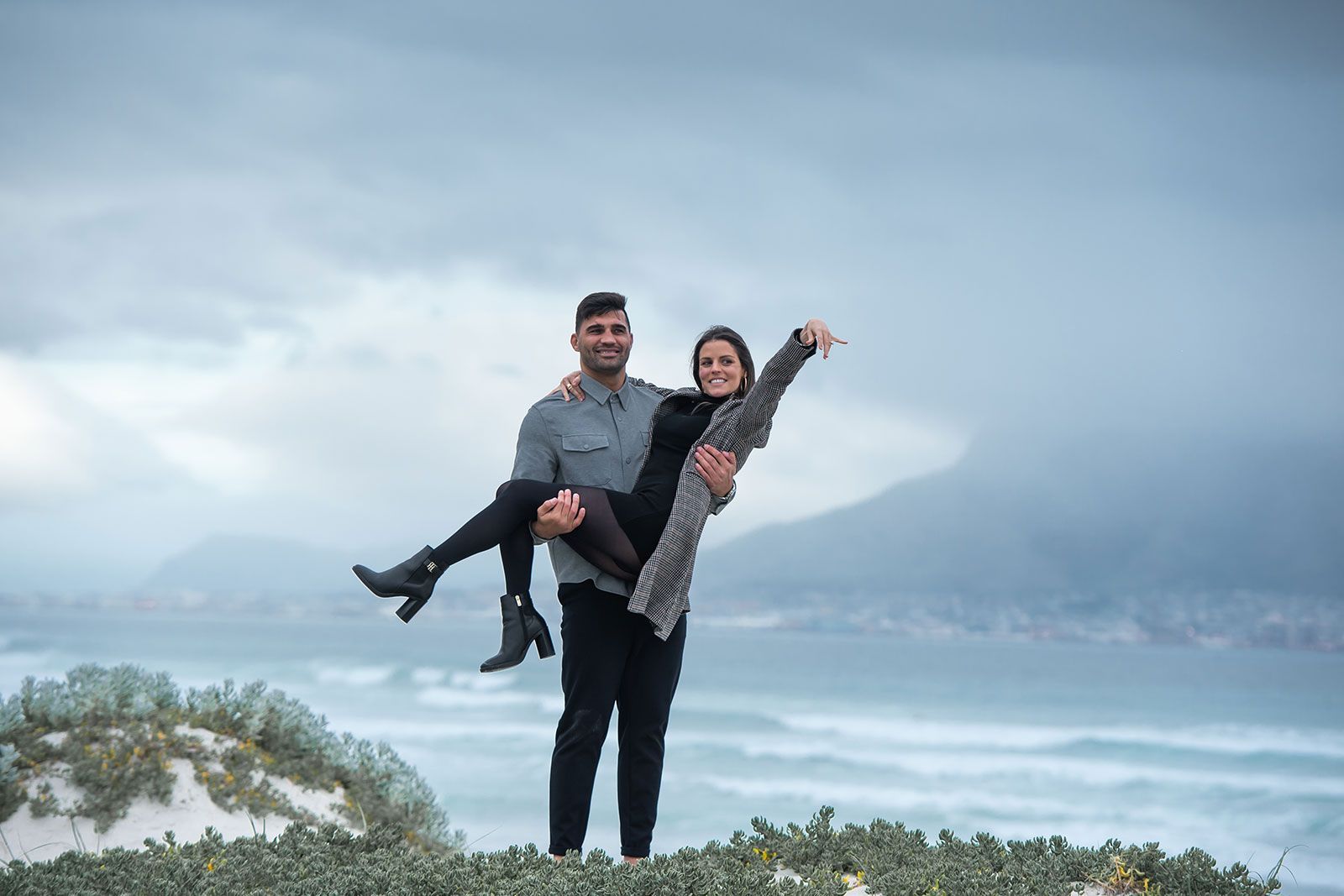 A man is holding a woman in his arms on top of a hill.