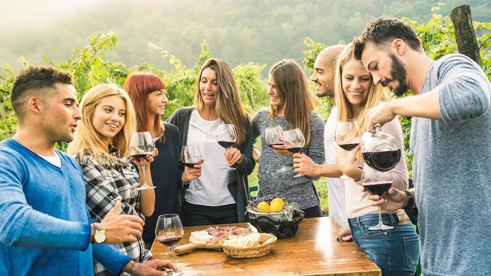 Eine Gruppe von Leuten steht mit Weingläsern in den Händen um einen Tisch herum.