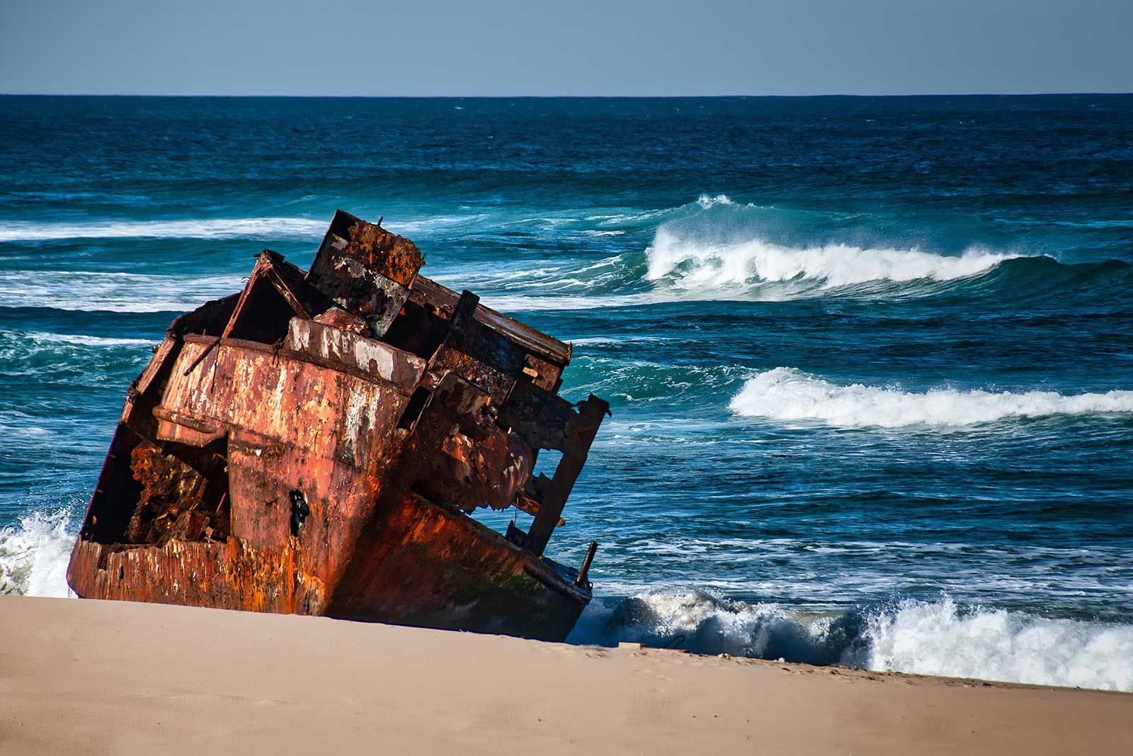 A rusty shipwreck is sitting on the beach near the ocean.