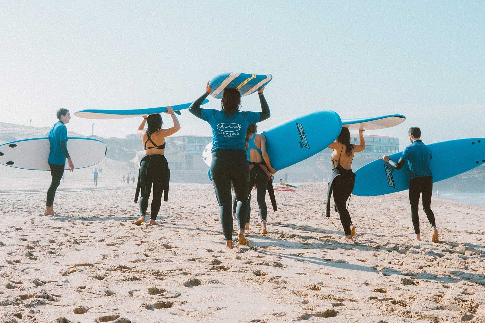 Un gruppo di persone che trasportano tavole da surf su una spiaggia.