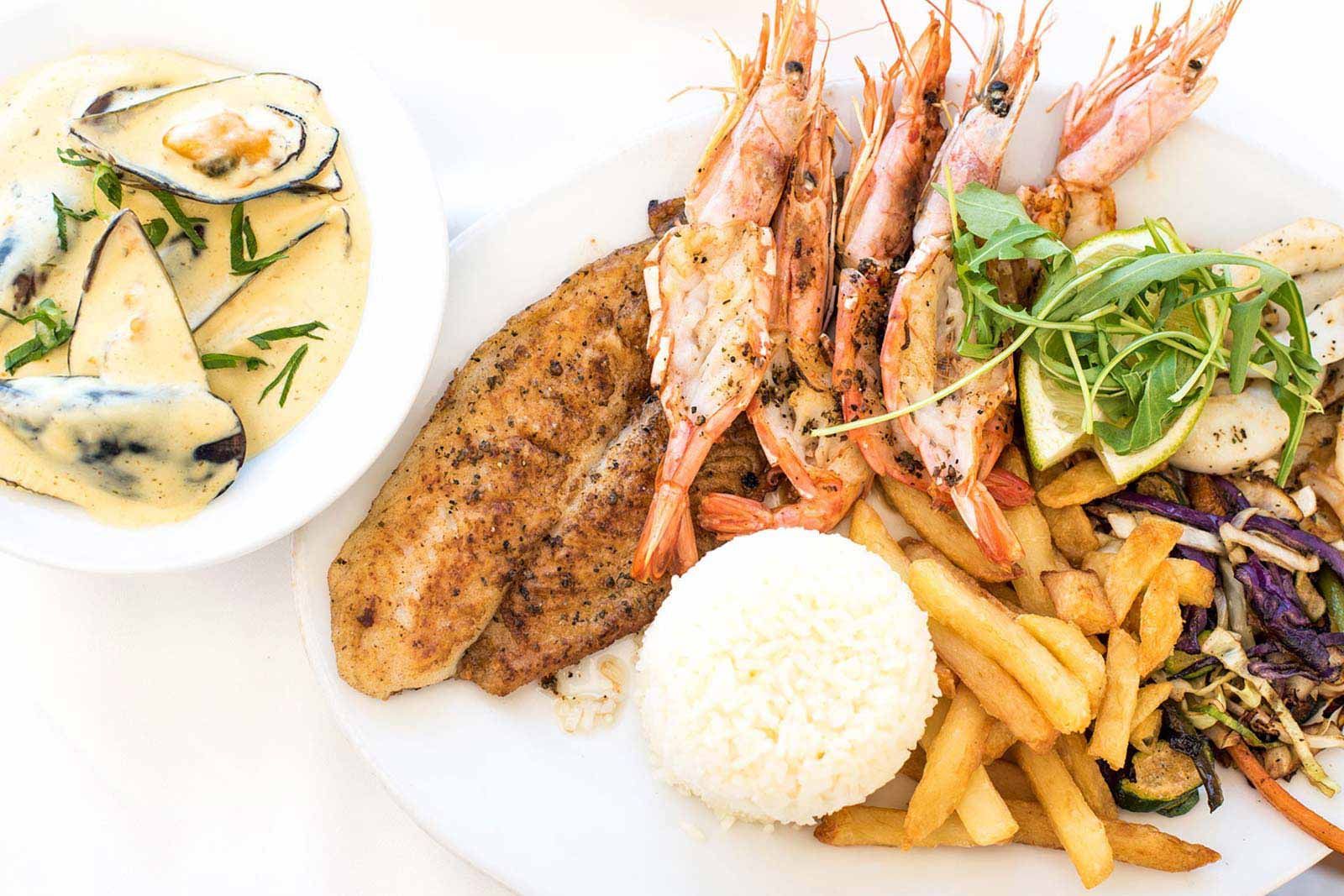 Un plato de comida con camarones, arroz y papas fritas en una mesa.