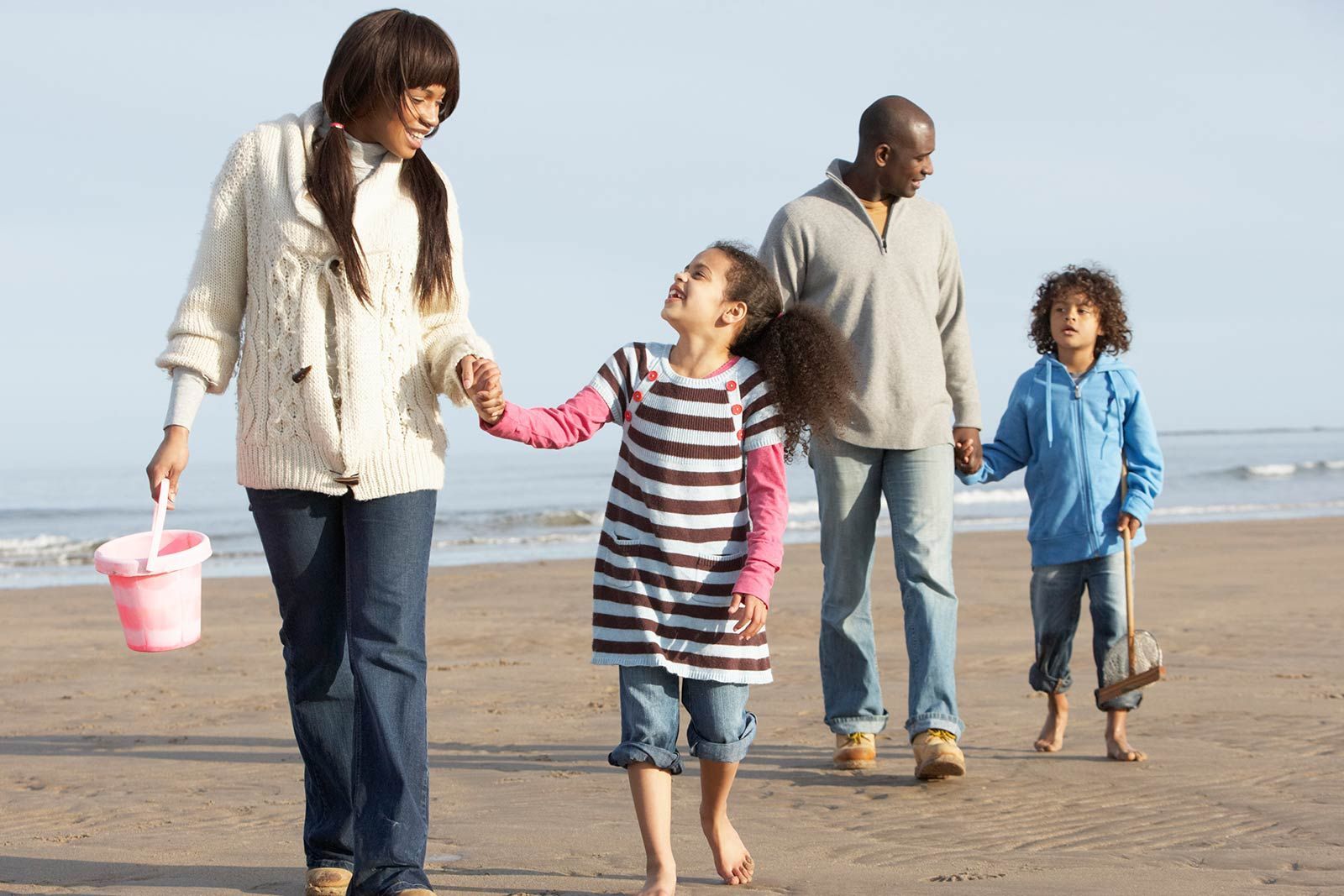 Eine Familie geht Händchen haltend am Strand spazieren.