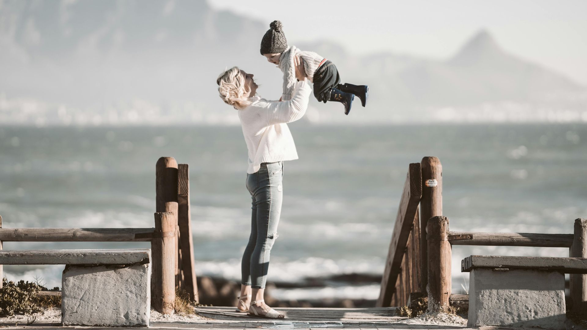 A woman is holding a child in her arms on a pier near the ocean in Cape Town
