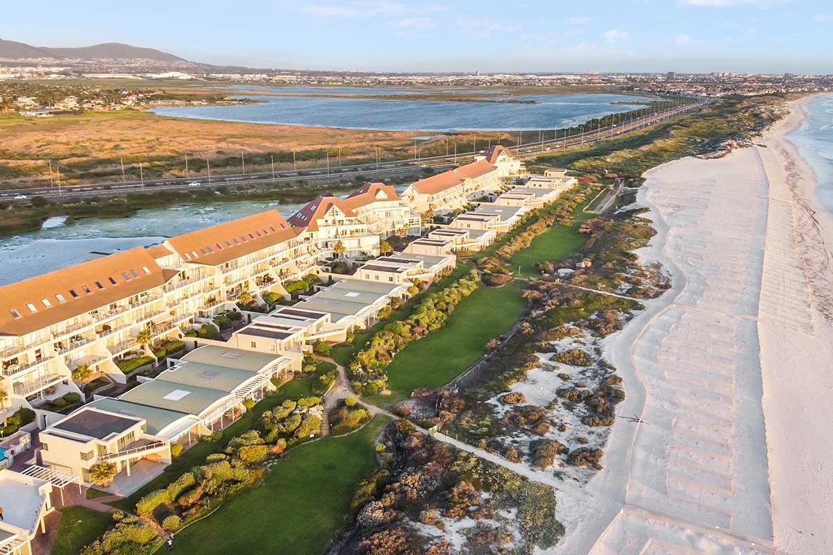 Een luchtfoto van een strand met een hotel op de achtergrond.