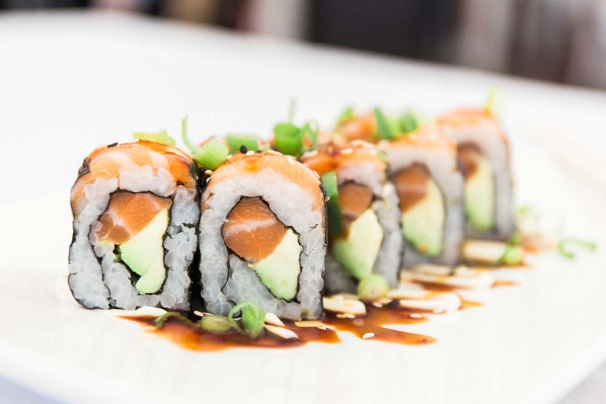 A row of sushi rolls with salmon and avocado on a white plate.