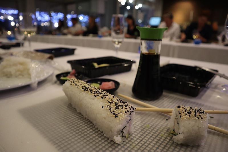 A sushi roll with chopsticks and a bottle of soy sauce on a table.