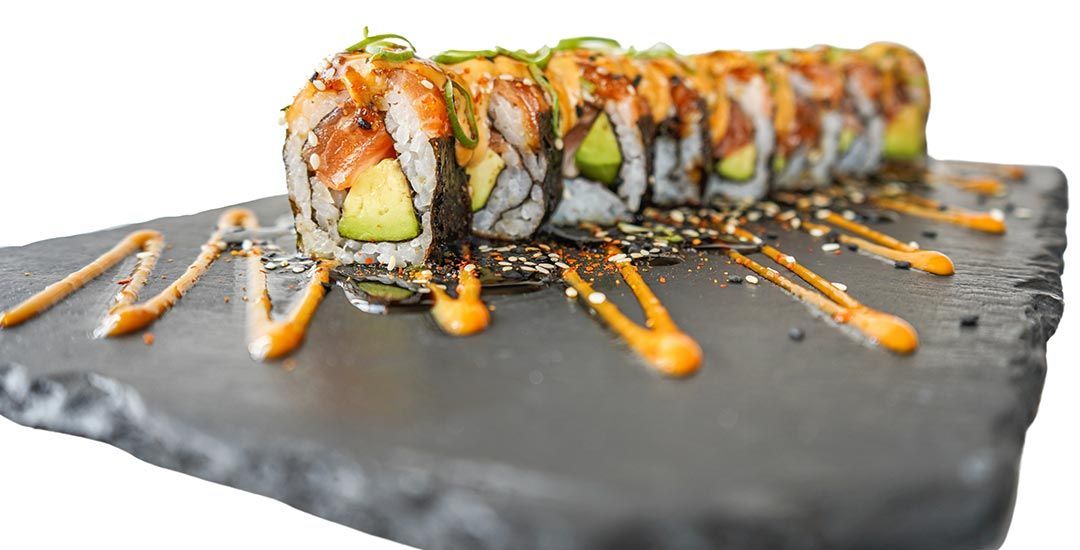 A close up of a sushi roll on a slate cutting board.