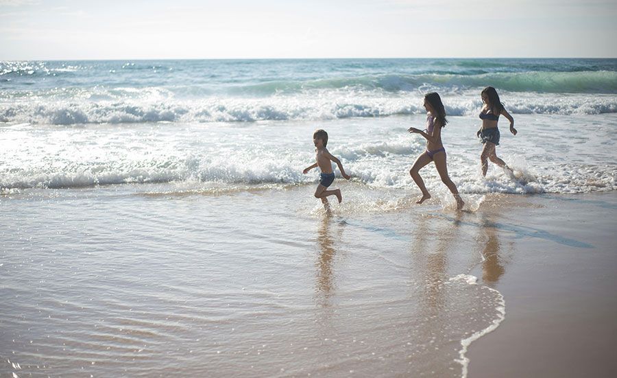 Eine Frau und zwei Kinder rennen am Strand entlang.