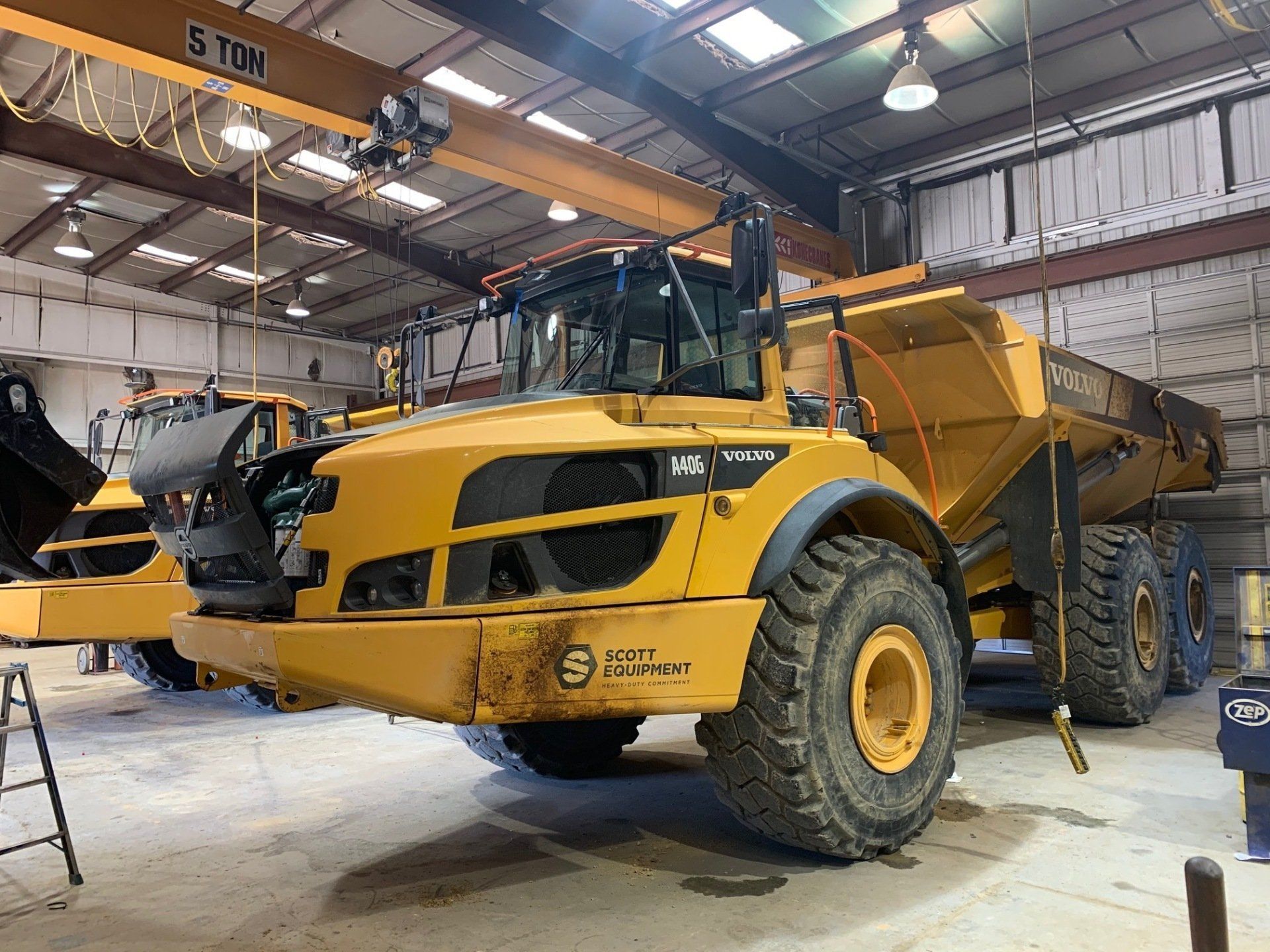 A yellow dump truck is parked in a garage under a crane.