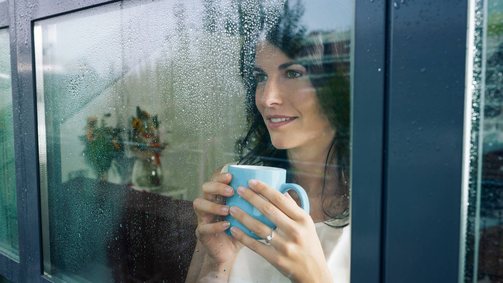 A woman is holding a cup of coffee and looking out of a window.