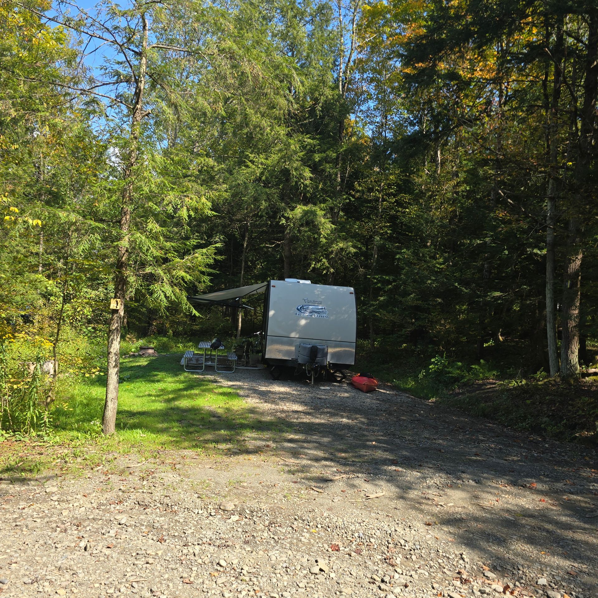 A travel trailer parked in a gravel campsite, surrounded by trees.